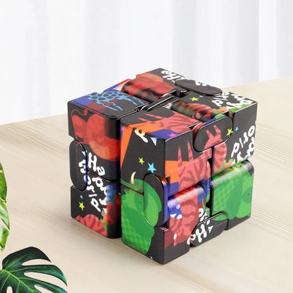 Infinity Magic Cube displayed on wooden surface, featuring colorful graffiti-style design in red, green, blue, and black. The cube shows interconnected segments that can be folded and transformed, with vibrant street art patterns and star designs decorating its surfaces.