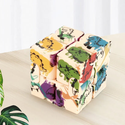 Infinity Magic Cube featuring colorful dinosaur patterns on cream-colored blocks arranged in a 3x3 cube formation, displayed on a wooden table with green plants in the background. The cube showcases playful cartoon dinosaurs in yellow, green, blue, and purple colors.