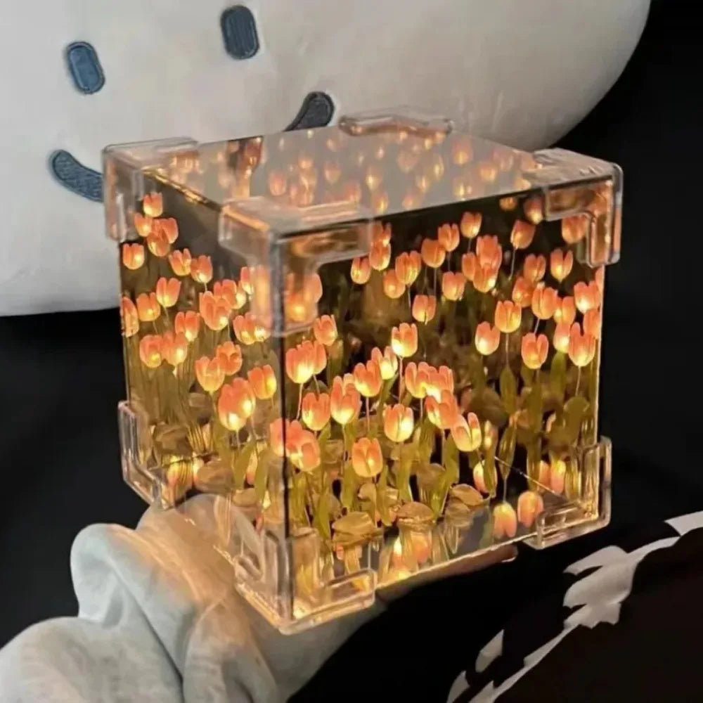 Creative Tulip Flower Sea Cube: A transparent cube-shaped night light displaying illuminated orange tulips in a sea-like arrangement, creating a warm, ethereal glow through its clear acrylic walls, held against a dark background.