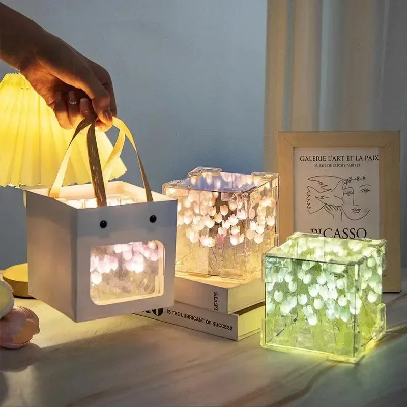 Creative Tulip Flower Sea Cube night lights displayed in illuminated cubes, showcasing three different color variations - yellow, warm white, and green. Each cube features delicate tulip flower patterns creating a glowing underwater effect, with a hand adjusting one of the portable lights.