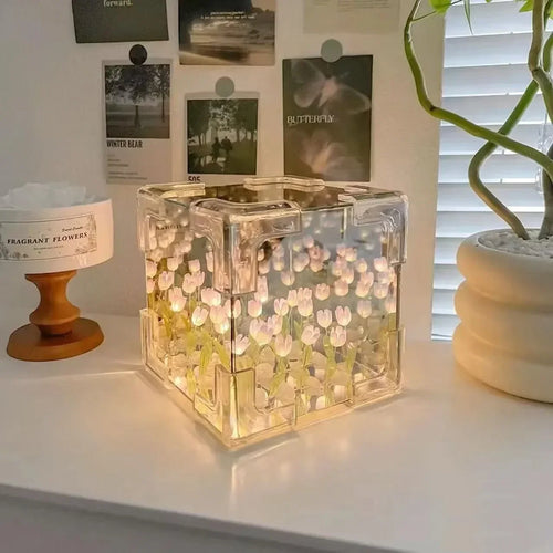 Creative Tulip Flower Sea Cube: Illuminated glass cube lamp featuring delicate white tulip designs glowing against a dark background, creating an ethereal underwater effect. The transparent cube sits on a white surface, casting a warm, ambient light in a minimalist setting.