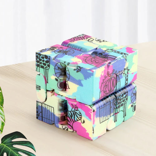 Infinity Magic Cube featuring vibrant tie-dye pattern with playful animal designs in pastel blue, pink, and yellow colors, displayed on wooden surface. Cube shows multiple segments for endless folding and transformation, showcasing its fidget-friendly design.