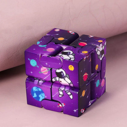 Infinity Magic Cube in purple with space-themed design featuring astronauts, planets, and stars on each segment, displayed against a pink background. The cube shows its unique foldable structure with interconnected panels in metallic finish.