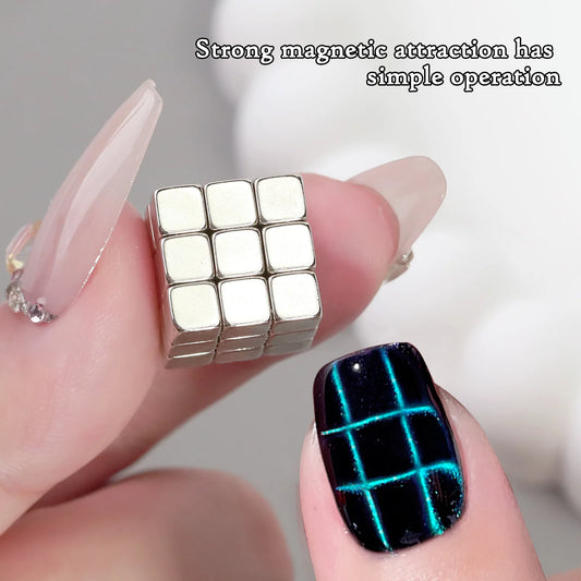 A small cube made of metallic magnetic blocks is held between two fingers with elegant nail art. One nail features a glossy black polish with a glowing blue grid pattern, while the other has a clear, nude-tone design with rhinestone embellishments. The background is blurred, and a caption at the top reads, "Strong magnetic attraction has simple operation.